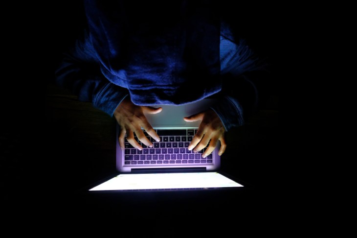 Hooded hacker Man with laptop stealing personal data from internet